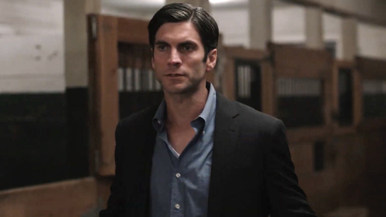 Wes Bentley as Jamie Dutton wearing a black suit, with a dark blue shirt and graying black hair. He's stood in a stable.
