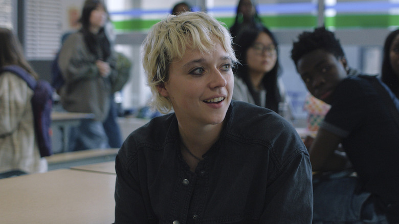 Thalia Dudek as Emaline sitting in the middle of a cafeteria looking amused in a scene from "Carrie."