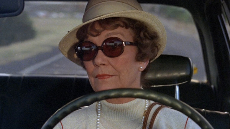 head-on view through windshield of Eleanor Willard in hat and sunglasses driving car