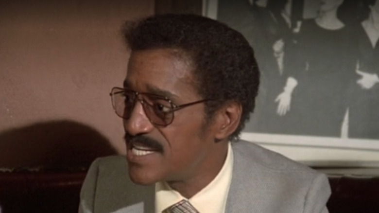 Sammy Davis, Jr. in grey suit sitting at restaurant table