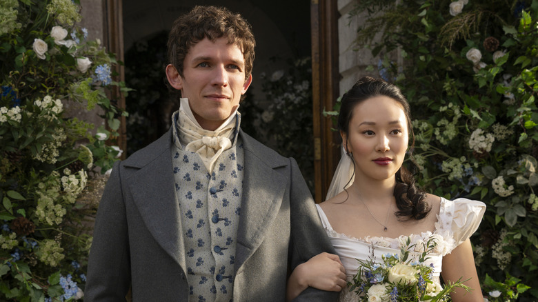 Alfie (David Moorst) and Sophie (Yerin Ha) walking down the aisle at her wedding wearing regency attire in the series "Bridgerton."