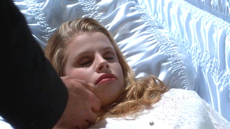 A hand caressing a corpse in an open casket
