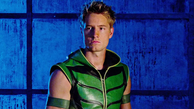 Justin Hartley in a sleeveless green and black leather hooded jacket. He has spiky blond hair.