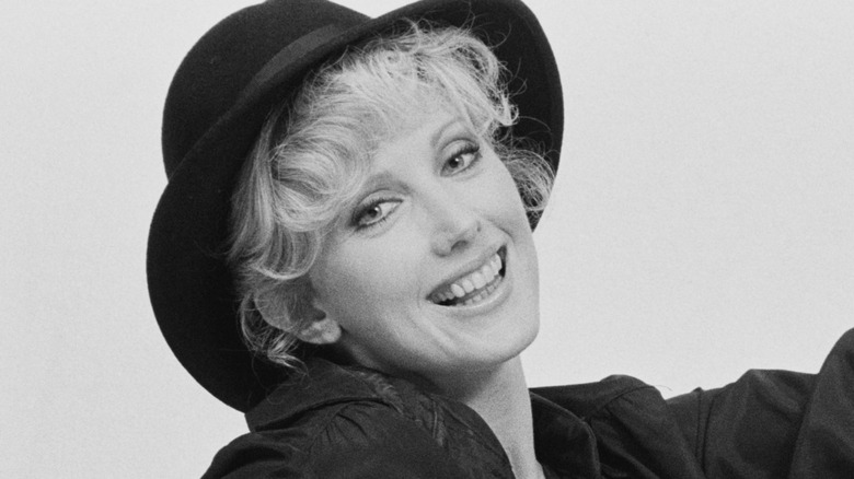 Morgan Fairchild smiling and wearing a hat