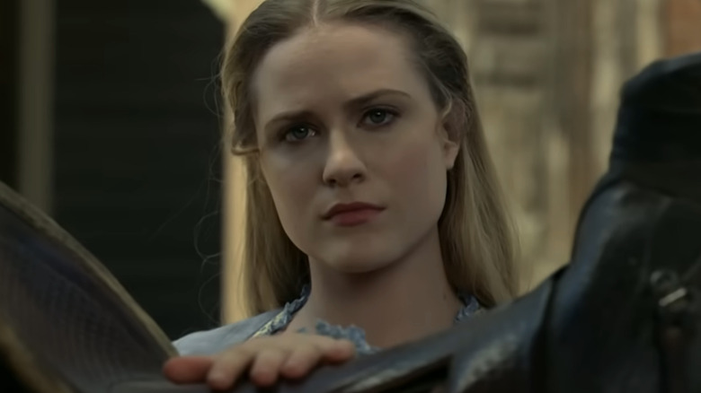 Dolores Abernathy looking over a horse's saddle out at someone in the park on Westworld