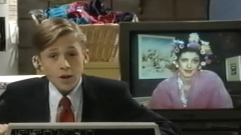 Ryan Gosling wearing a suit jacket and tie and sitting next to a TV monitor during a scene from "The All-New Mickey Mouse Club."