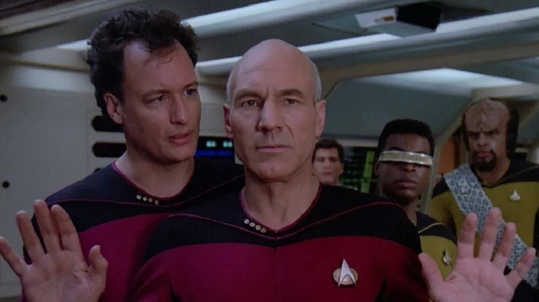 Q wearing a Starfleet uniform and speaking to Jean-Luc Picard with Geordi LaForge and Worf in the background on Star Trek: The Next Generation