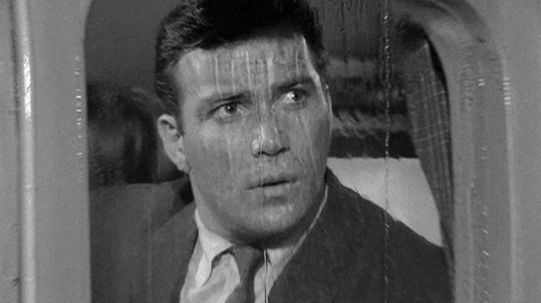 Bob Wilson looking out a rainy plane window from his seat on the flight in The Twilight Zone