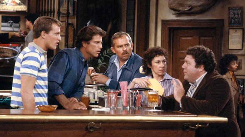 Woody Boyd, Sam Malone, Cliff Clavin, and Carla Tortelli looking at Norm Peterson as he tells a story around the bar on Cheers