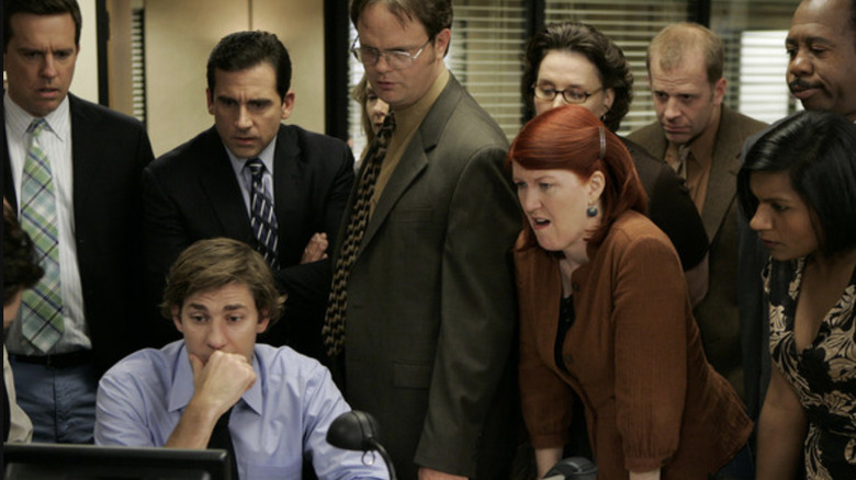 Andy Bernard, Michael Scott, Jim Halpert, Dwight Schrute, Phyllis Vance, Meredith Palmer, Toby Flenderson, Stanley Hudson, and Kelly Kapoor looking at something on Jim's desk computer in The Office