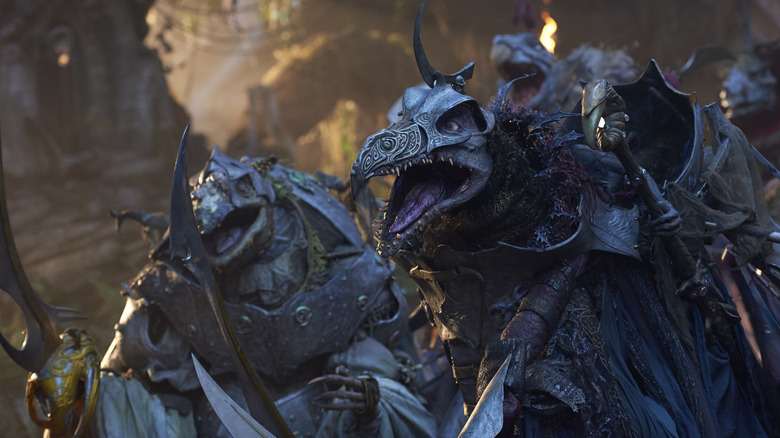 Several armored creatures with beaks holding staffs and roaring at something off-camera.