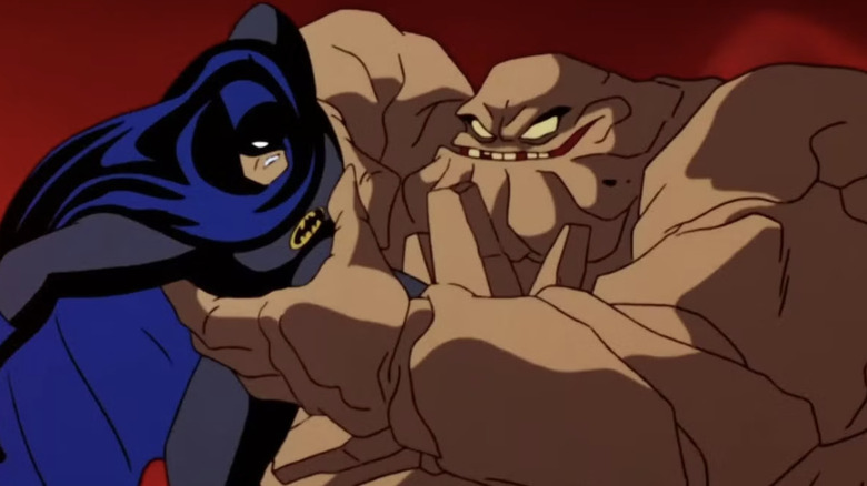 Batman wearing a gray suit with a black/blue cape and white eyes. He's been caught by Clayface, a giant brown sludge monster with yellow eyes.