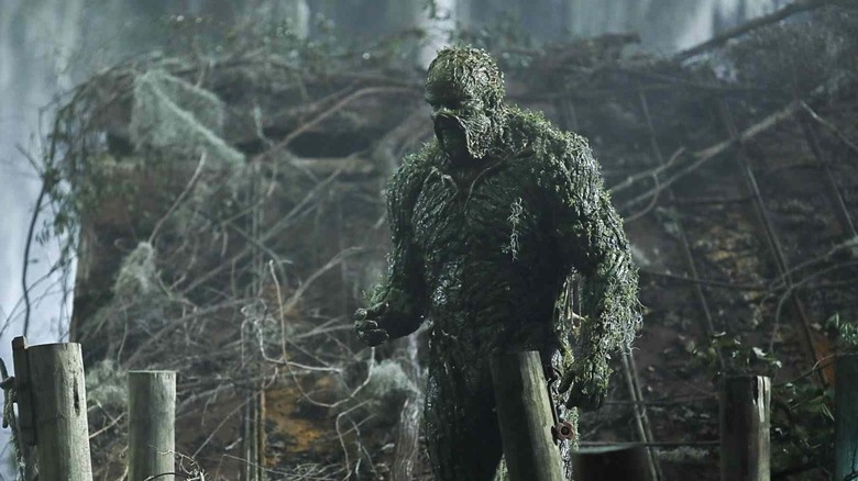 Derek Mears as Swamp Thing standing in a swamp.