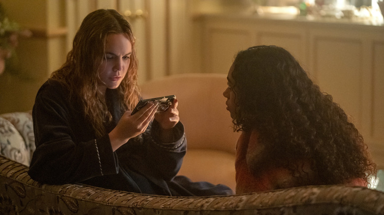 Bailee Madison as Imogen Adams holding a phone while sitting across from Chandler Kinney as Tabby Haworthe in "Pretty Little Liars: Original Sin."