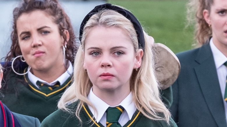 Erin wearing green school uniform in front of a crowd of students in similar outfits in "Derry Girls."