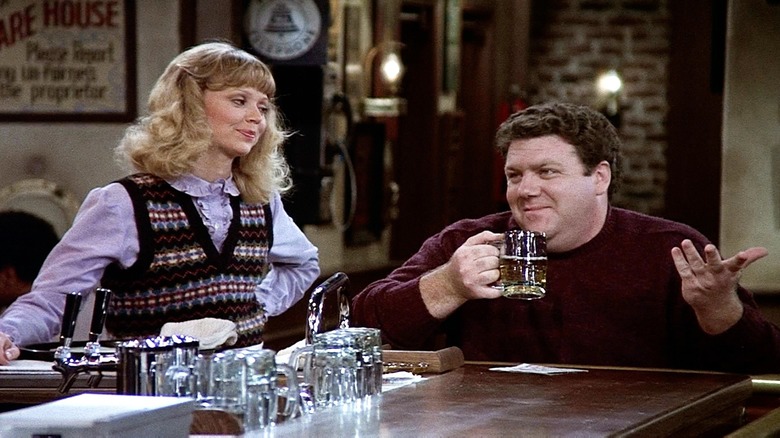 Diane smirking as Norm enjoys a beer in "Cheers"