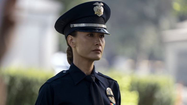 Maggie Q as Renée Ballard wearing a navy blue police officer's uniform complete with a hat.