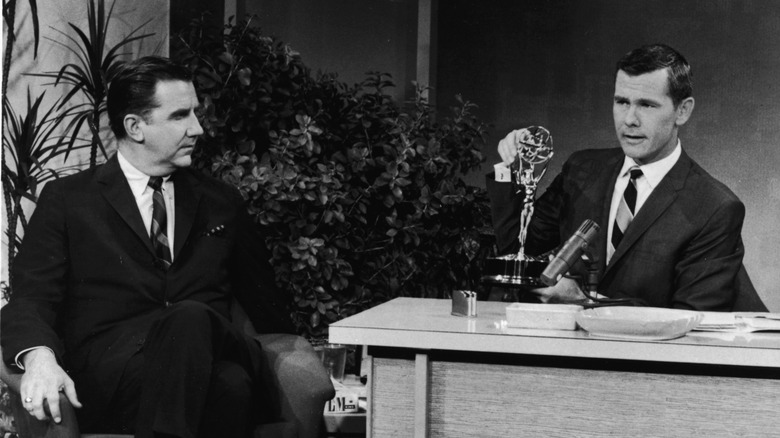 Announcer Ed McMahon sits in a guest chair next to host Johnny Carson at his desk with an Emmy on it
