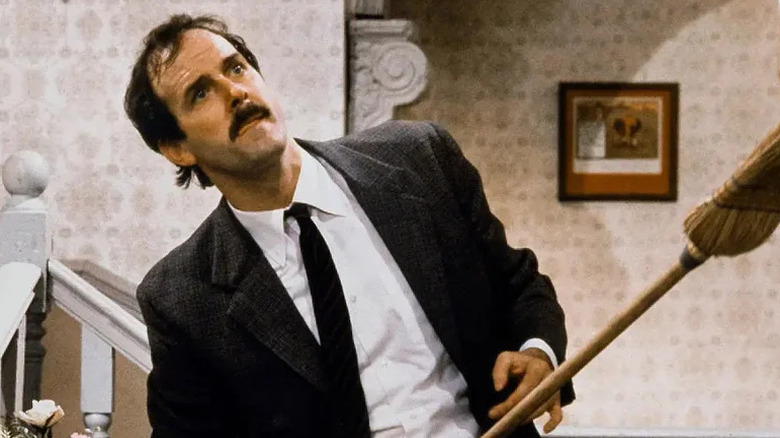 Basil Fawlty in suit holding broom in "Fawlty Towers" (1975-1979)