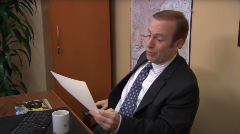 Bob Odenkirk's Mark sits at a desk reading a sheet of paper in The Office