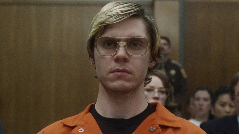 Jeffrey Dahmer staring blankly ahead while wearing large glasses and an orange prison jumpsuit in Dahmer