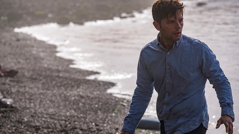 A soaked Jordan Sanderson (Adam Scott) walks by a beach in The Twilight Zone