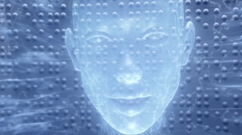 A blue holographic display of a woman in a futuristic laboratory. She has no hair and no detail in her eyes.