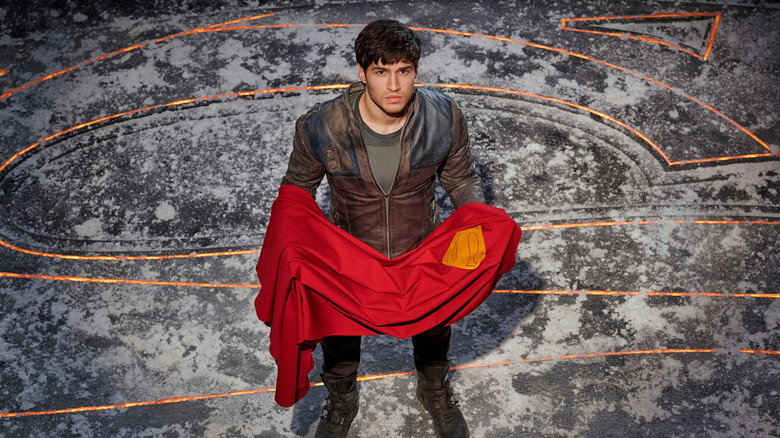 Cameron Cuffe as Seg-El, looking up and holding Superman's cape in Krypton.