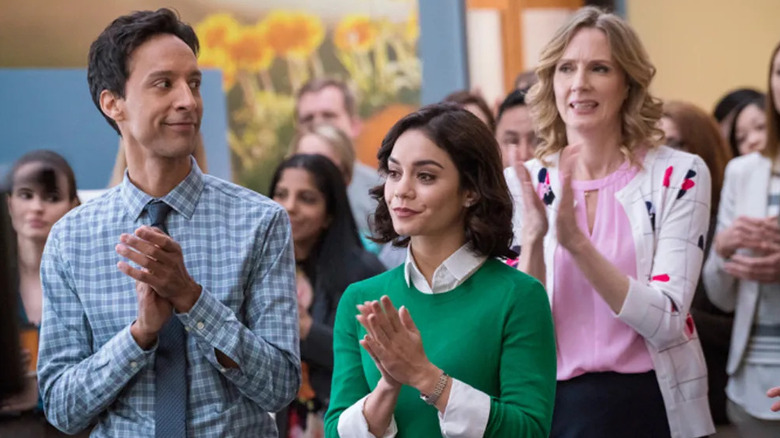 Danny Pudi as Teddy and Vanessa Hudgens as Emily Locke, clapping with their coworkers in Powerless.