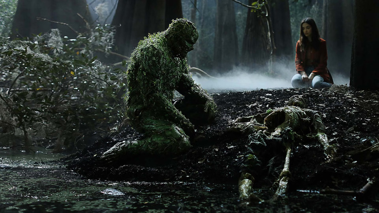 Derek Mears as Swamp Thing, looking over a skeleton in Swamp Thing.