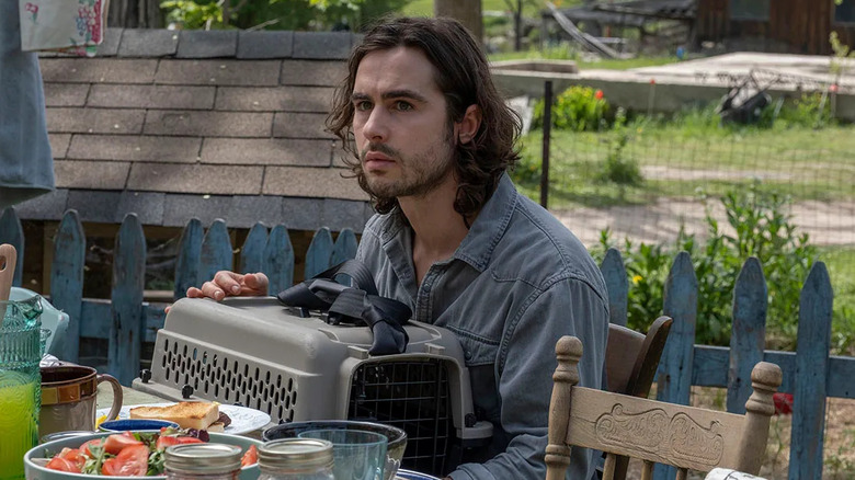Ben Schnetzer as Yorick Brown, sitting at a table with a crate in Y: The Last Man.