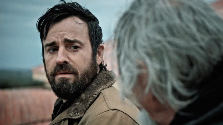 Justin Theroux as Kevin Garvey with messy dark hair and a beard. He's wearing a brown coat and is looking at a man with long gray hair on the right of the image.