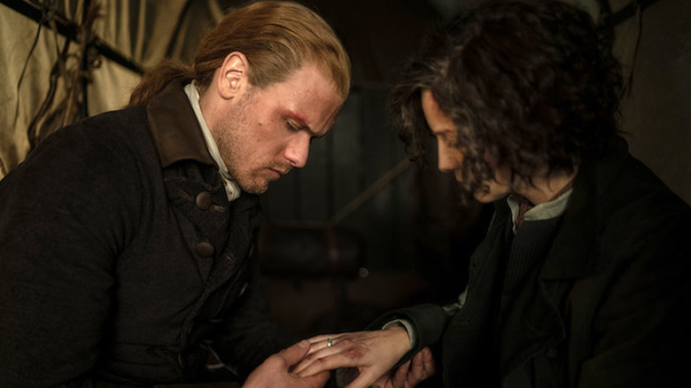 Jamie Fraser (Sam Heughan) examines the bruised knuckles of Claire Fraser (Caitríona Balfe) in Outlander
