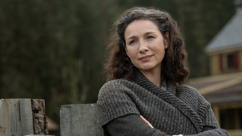 Claire Fraser (Caitríona Balfe) smiles wistfully by a wooden fence in Outlander