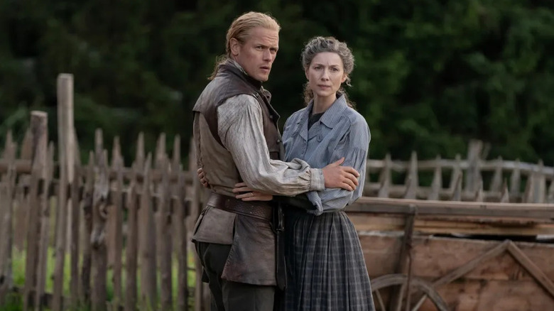 Jamie Fraser (Sam Heughan) and Claire Fraser (Caitríona Balfe) embrace by a fence in Outlander