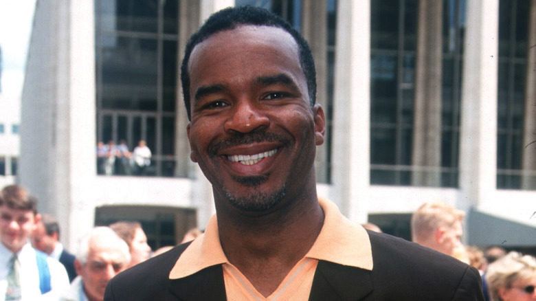 Kahverengi bir ceket ve şeftali rengi yakalı gömlek giyen David Alan Grier, dışarıda bir tanıtım etkinliğinde gülümsüyor