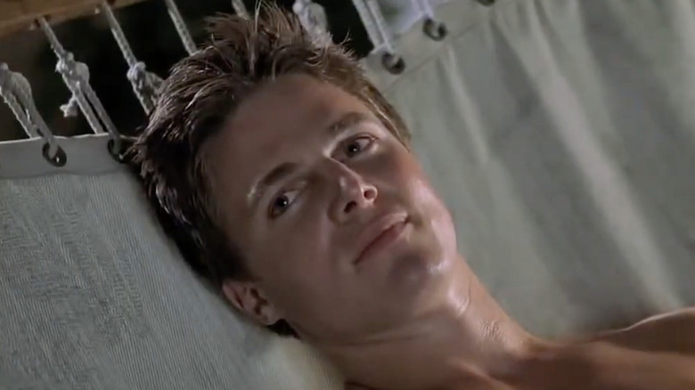 A shirtless Stephen Amell is lying on a white hammock. He has short brown hair and is looking up to the left.