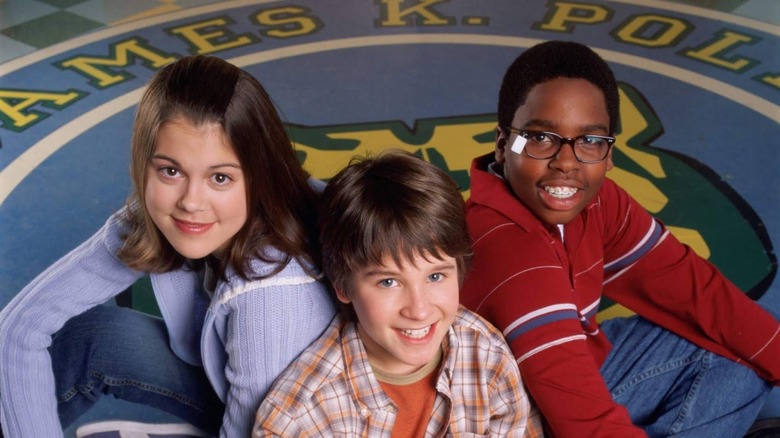 From left, Jennifer "Moze" Mosley (Lindsey Shaw), Ned Bigby (Devon Werkheiser), and Simon "Cookie" Nelson-Cook (Daniel Curtis Lee) sit together above the crest for their middle school in Ned's Declassified School Survival Guide