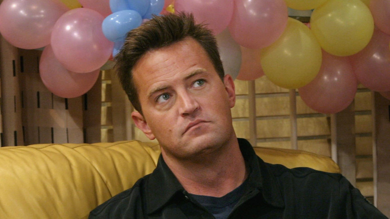 Matthew Perry playing Chandler Bing sitting on a yellow couch in front of balloons on the set of Friends