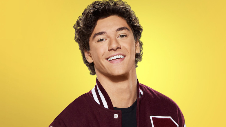 Jamie Spano kırmızı bir üniversite ceketi giyiyor ve Saved by the Bell'in yeniden başlatılması için bir karakter posterinde sarı bir arka planın önünde gülümsüyor
