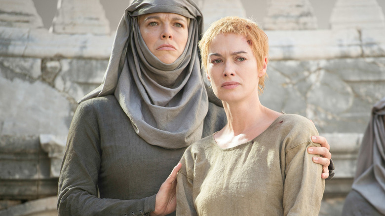 Septa Unella in gray robes holding a shorn-headed Cersei Lannister, who has a cut on her forehead.