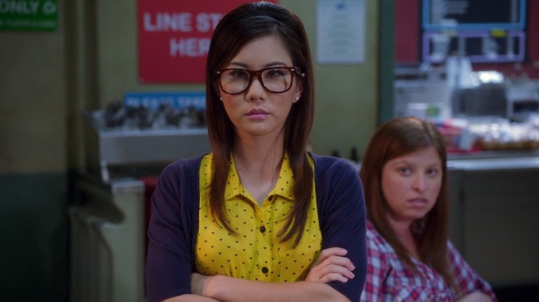 Annie Kim stands with her arms crossed at Greendale Community College's cafeteria
