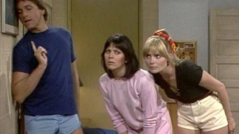 Jack Tripper (John Ritter) listens closely to a wall, joined by Janet Wood (Joyce DeWitt) and Terri Alden (Priscilla Barnes) in Three's Company
