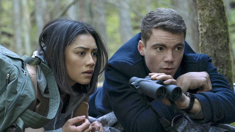 Luciane Buchanan as Rose laying on the ground next to Gabriel Basso as Peter, holding binoculars, in "The Night Agent."