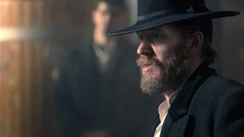 Alfie stood with his nephew in the background against a barrel in Peaky Blinders