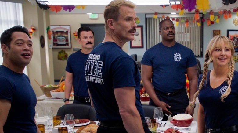 The cast of Tacoma FD in blue firefighter shirts standing around Thanksgiving table