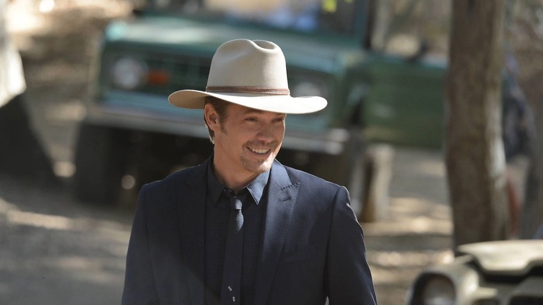 Raylan Givens (Timothy Olyphant) smiles while walking between cars in Justified