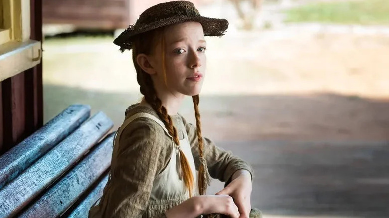 Amybeth McNulty as Anne Shirley sitting in bench in hat in Anne with an E