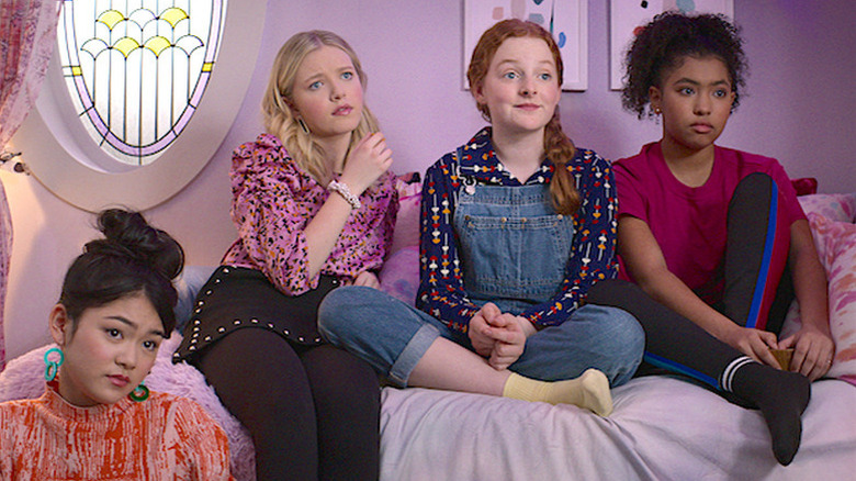 Momona Tamada as Claudia, Shay Rudolph as Stacey, Vivian Watson as Mallory, and Anais Lee as Jessi sitting in pink bedroom in The Baby-Sitters Club