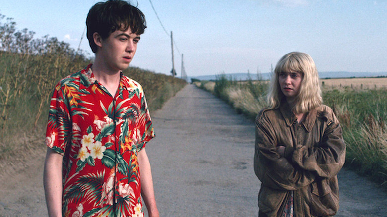 Alex Lawther as James in red Hawaiian shirt standing on road next to Jessica Barden as Alyssa in brown coat The End of the F***ing World